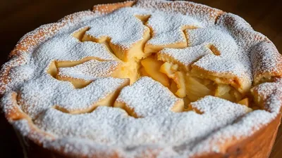 Frischer Apfelkuchen mit Puderzucker bestreut, goldbraun gebacken, auf Teller.